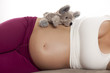 © vladimirfloyd - pregnant woman lying on a bed with plush toy on white background
