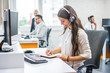 © Bojan - Smiling woman operator agent with headset taking notes while talking with client in call center