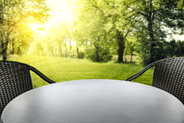 Wall Mural - empty round table with copy space for products and two black chairs with green trees ans sunshine su