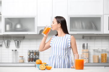 Poster - Young woman drinking orange juice in kitchen