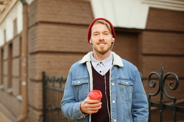 Wall Mural - Portrait of hipster with earphones listening to music and drinking coffee outdoors