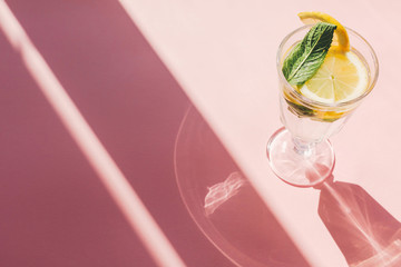 summer vacation and party concept. fresh cocktail with lemon and mint in vintage glass on trendy pink paper background in sun light. mojito. refreshing drinks. space for text