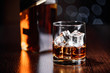 A glass of whiskey on the rocks and a bottle on the table on a dark background with a bokeh