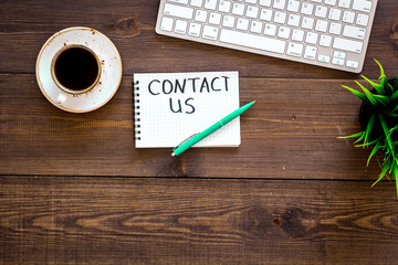 Poster - Template for contacts, background for contact information. Lettering Contact us in notebook on office work desk with computer on dark wooden background top view space for text