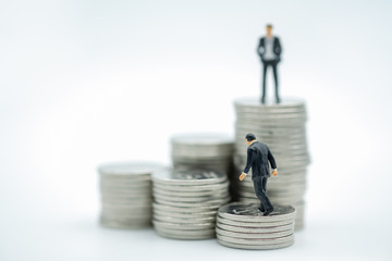 Business Money and saving concept. Businessman miniature figure walking on stack of coins with another  man on top of stack on white background.