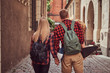 Back view of a young hipster couple, handsome skater and his girlfriend, holding hands, walking around a old narrow streets of Europe.