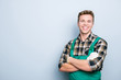 Portrait of kind cheerful excited smart professional friendly expert handsome with beaming shiny smile handyman wearing green overalls standing with folded hands isolated on gray background copyspace