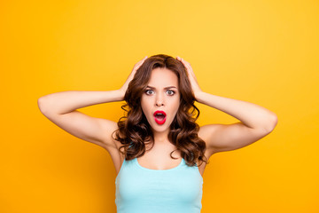 WTF! Portrait of irritated impressed woman holding two hands on head keeping wide open mouth looking at camera isolated on yellow background