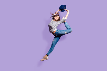 Wall Mural - Portrait of active pretty girl in action jumping in the air showing perfect stretching making athletic ballet pose trick isolated on violet background holding hat in hands enjoying dreamday
