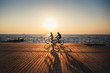 © Iryna Budanova - Couple of young hipsters cycling together at the beach at sunrise sky at wooden deck summer time