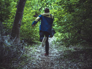 young scary man running away in the dark forest on the path back view