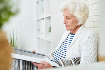 Wall Mural - Side view portrait of elegant senior woman opening box of photos and cherished little things remembering her family and friends while sitting alone at home in modern apartment.