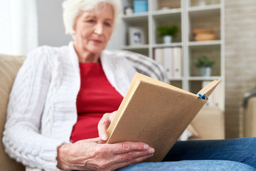 Wall Mural - Low angle portrait of white-haired woman reading book while enjoying leisure time at home, focus on book in wrinkled hands, copy space