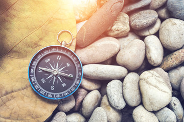 Navigation compass on old leaf and stone pebbles with sunlight. Travel background concept.