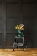 A Rich Colorful Bouquet Of Beautiful Summer Flowers In A Blue Glass Vase On A Black Step Stool In A Dark Living Room Interior