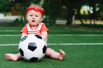 Little girl in sport shirt and red hair band playing with a soccer ball at football field. Summer kid sport concept