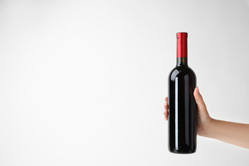 Sticker - Woman holding bottle of expensive red wine on light background