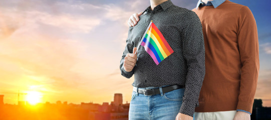 gay pride, lgbt and homosexual concept - close up of happy male couple with rainbow flags over city sunset background