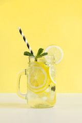 Wall Mural - Fresh summer fruits water or lemonade with lemon and mint on yellow background. Close up.