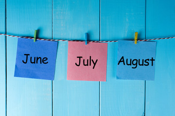 Sticker - Three summer month - June, July and August - on notes pinned at wooden wall. Summer calendar concept