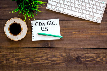 Poster - Template for contacts, background for contact information. Lettering Contact us in notebook on office work desk with computer on dark wooden background top view space for text