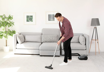 Sticker - Young man removing dirt from carpet with vacuum cleaner at home