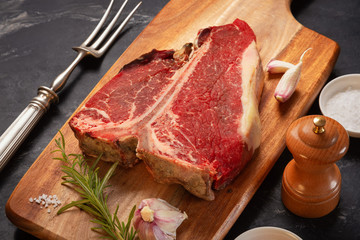 Wall Mural - Meat for a barbecue. One raw piece of beef meat on the bone. steak t bone, salt, spices on a wooden kitchen board top view. The best piece of meat eight weeks maturation