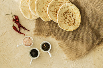 Poster - Top view of pita bread on burlap fabric, red chili peppers and cups with spices on a beige surface