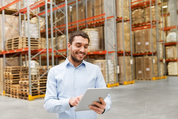 logistic business, technology and shipment concept - happy businessman with tablet pc computer checking goods at warehouse