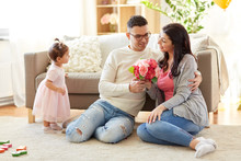 Family, Holidays And Greetings Concept - Happy Husband Giving Flowers To His Wife At Home