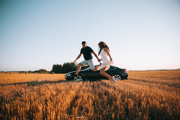 Wall Mural - Couple in the jump.A young couple jumps together on a summer day in the field.A couple in the jump on the background of cars.Summer fun days.Couple in love