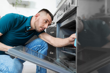 Wall Mural - household and people concept - man wiping table with cloth cleaning inside oven at home kitchen