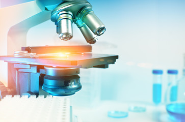 scientific background with closeup on light microscope and laboratory out of focus