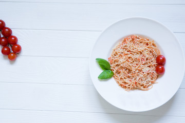 Tomato pasta wish cheese, basil, red cherry tomatoes and basil leaf on white wooden background. Tasty italian cuisine, top view. Spaghetti with parmesan on rustic wooden background. Copy space.