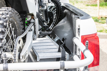 Rear viwe with two dirt bike motorcycles on the back of the truck with safety gear in residential setting.