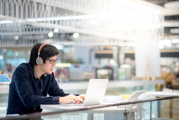 Young Asian business man listening to music by headphones while working with laptop computer in co working space. freelance or digital nomad lifestyle in urban workspace concepts