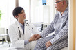 © Monet - 医療用ベッドで医師の診断を受ける高齢者の男性。
