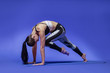 © Paul - Long haired beautiful pilates or yoga athlete does a graceful pose while wearing a tight sports outfit against a bright blue background in a studio