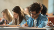 © Gorodenkoff - Shot of a Row of Multi Ethnic Students in the Classroom Taking Exam/ Test. Focus on Holding Pens and Writing in Notebooks. Bright Young People Study at University.