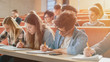 © Gorodenkoff - Row of Multi Ethnic Students in the Classroom Taking Exam/ Test/ Writing in Notebooks. Bright Young People Study at University.
