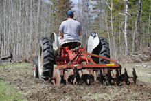 A Man Driving A Tractor Pulling A Farm Implement.