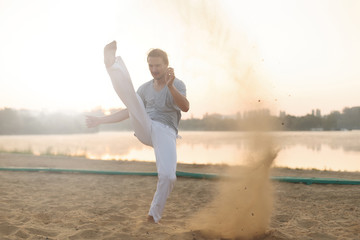 Wall Mural - Athletic capoeira performer workout training on the beach sunris