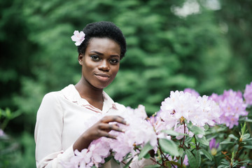 Wall Mural - Young black woman with afro hairstyle in urban park. Afro american girl wearing casual clothes between purple flowers.