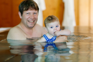 Wall Mural - Happy middle-aged father swimming with cute adorable baby girl in swimming pool.