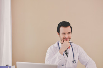 Wall Mural - Smiling doctor posing in the office, he is wearing a stethoscope, medical staff on the hospital background