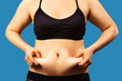 © vika33 - Body of young woman with excess weight, keeping your belly fat, isolated on blue background.