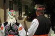 Kobieta i mężczyzna (górne części ciała), z tyłu, stoją, ubrani w odświętne łowickie stroje, pan w ozdobionym kwiatami kapeluszu, kobieta w wyszywanej w kwiaty chustce na głowie, czarne serdaki