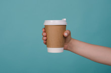 Coffee Cup In Woman Hand Isolated On Blue Background. Female Hand With Paper Cup. Mockup Of Female Hand Holding A Coffee Paper Cup. Copy Space