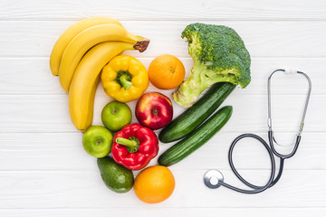 Wall Mural - top view of heart symbol made from fresh fruits and vegetables and stethoscope on wooden surface