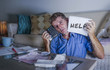 © TheVisualsYouNeed - young worried in stress man at home calculating month tax expenses with calculator accounting payments sad and depressed asking for help